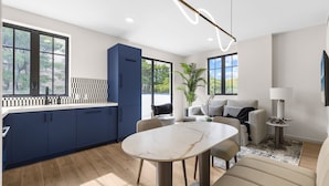 Una cocina moderna con armarios azul oscuro, una mesa de comedor de mármol y un ventanal grande.