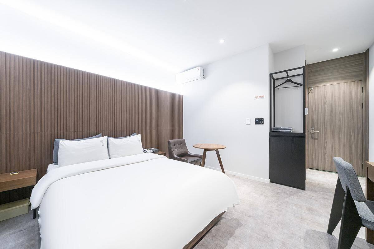 Una habitación de hotel moderna con una cama grande, una mesita, una silla, un armario y un espejo.