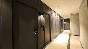 A hallway with dark-colored doors, each marked with a number and a small, illuminated sign. - Dubai Hotel Dangjin (Dangjin)