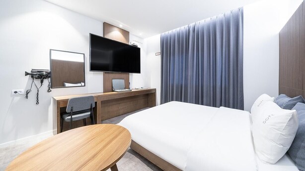 A modern hotel room with a bed, a desk, a chair, a television, and a large window with curtains. - Dubai Hotel Dangjin (Dangjin)