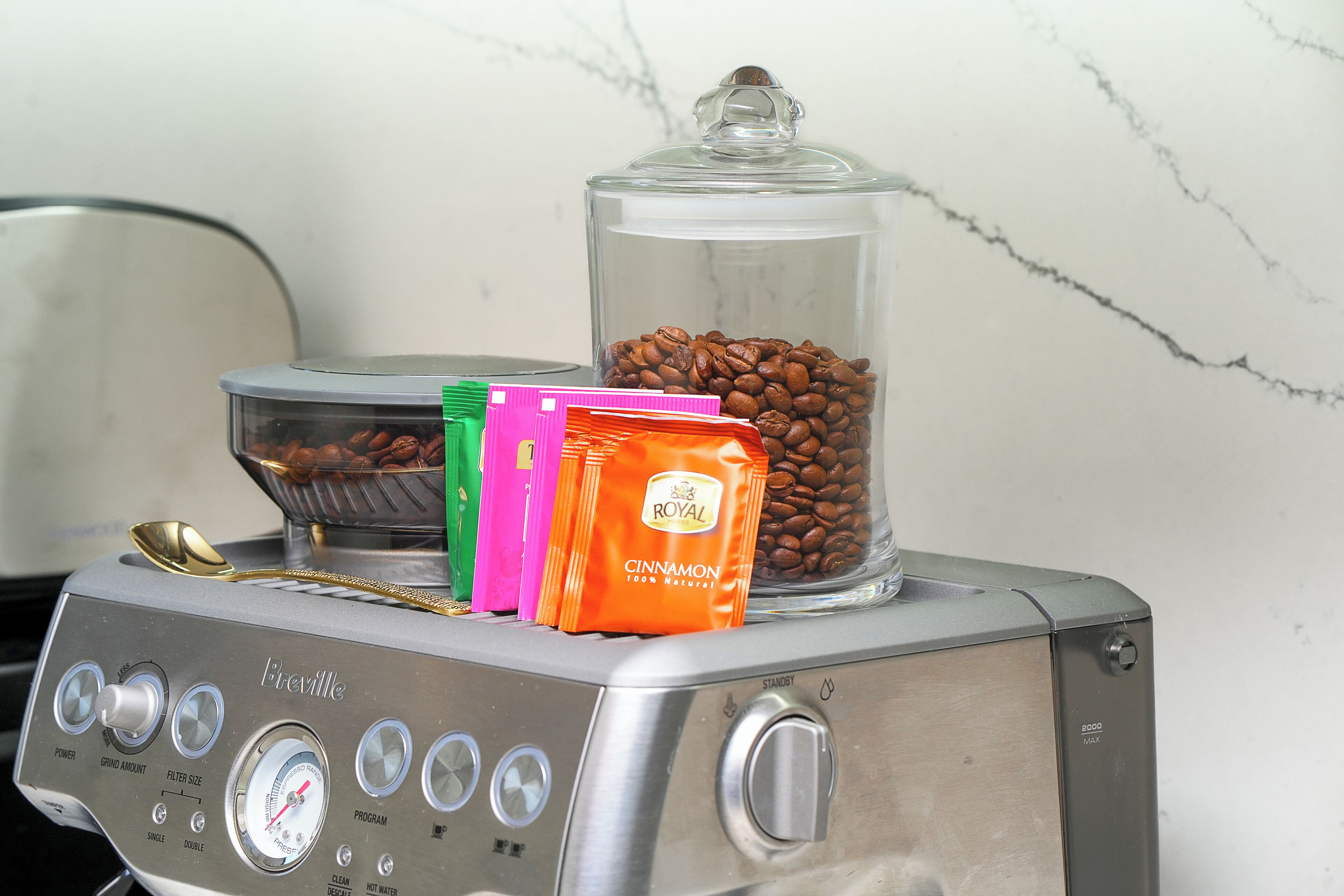 Una cafetera Breville con un molinillo de café, un recipiente de vidrio con granos de café y un paquete de canela.