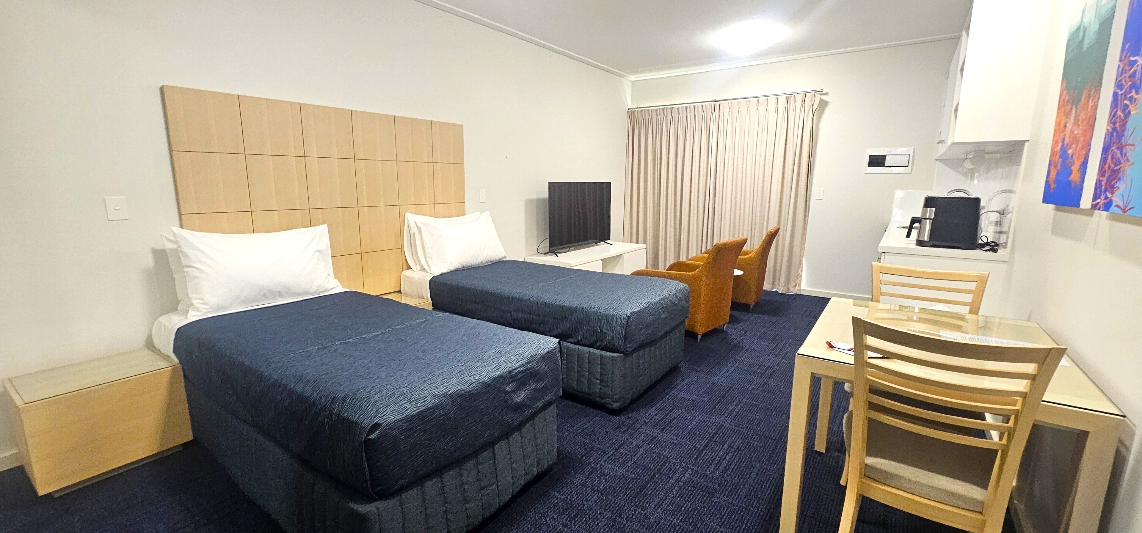 A hotel room with two beds, a desk, a chair, a television, and a coffee machine.