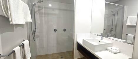 Un baño moderno con ducha envuelta en vidrio, un lavabo blanco y un espejo grande.