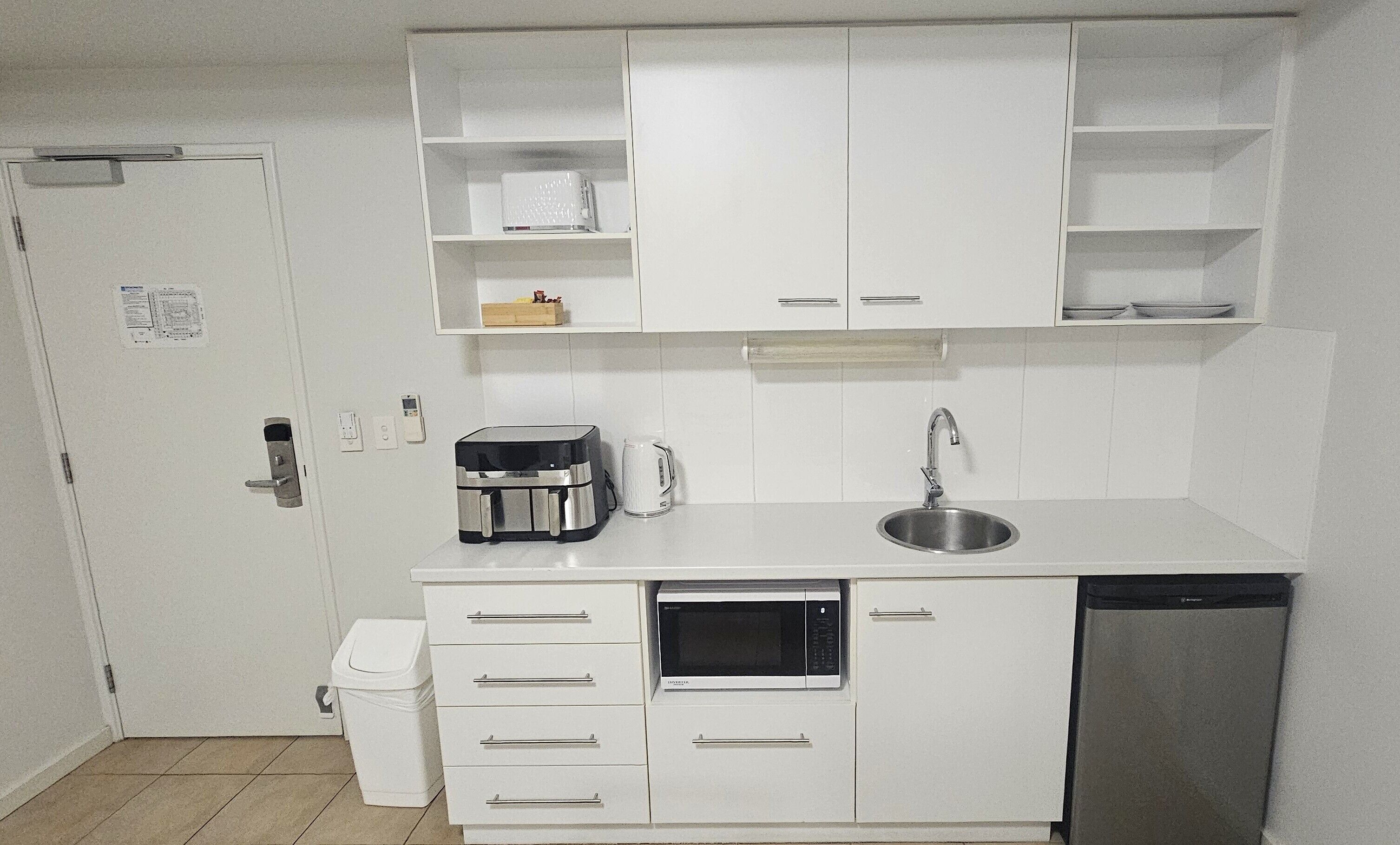 A compact kitchen with white cabinets, a built-in microwave, a coffee maker, a sink, and a dishwasher.