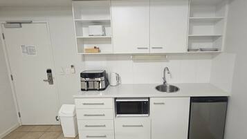 A compact kitchen with white cabinets, a built-in microwave, a coffee maker, a sink, and a dishwasher.