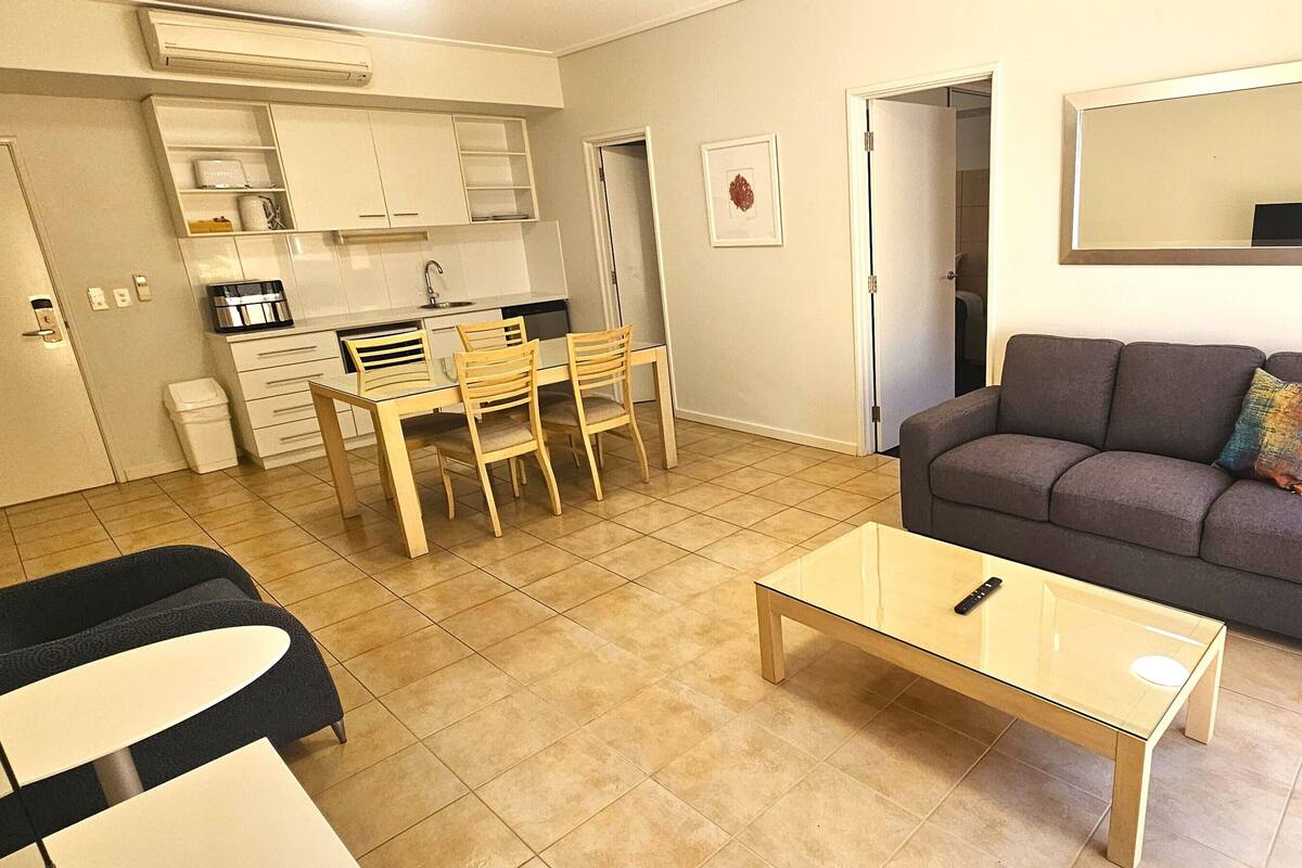 A compact living space with a kitchenette, a dining area, a sofa, and a glass coffee table.