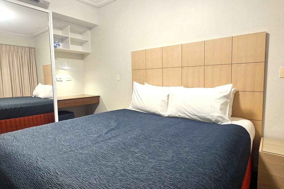 A hotel room with a large bed, a bedside table, a mirror, and a wardrobe.