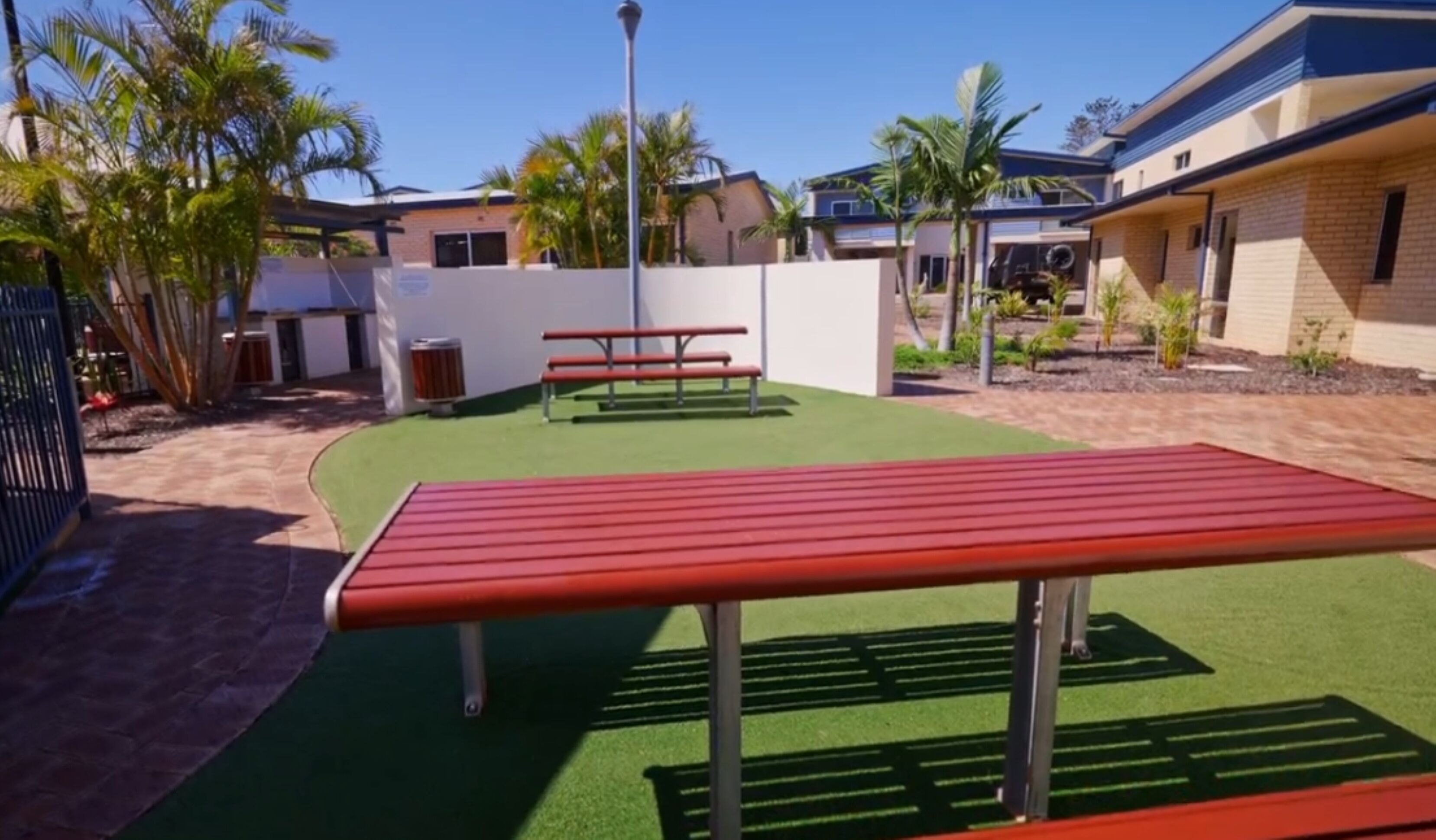 A courtyard with artificial grass, a red bench, and a trash can.
