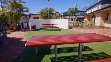 A courtyard with artificial grass, a red bench, and a trash can.