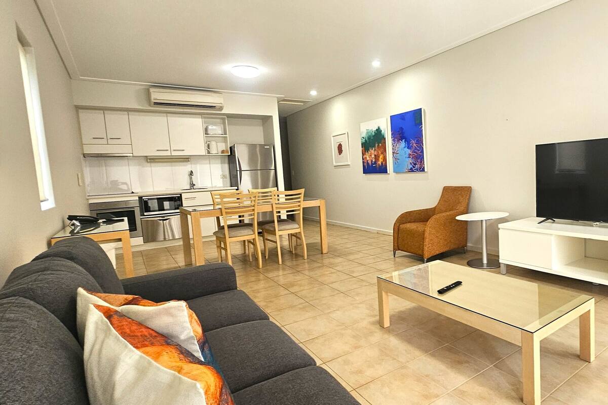 A modern living room with a sofa, coffee table, TV, and a dining area with chairs and a table.