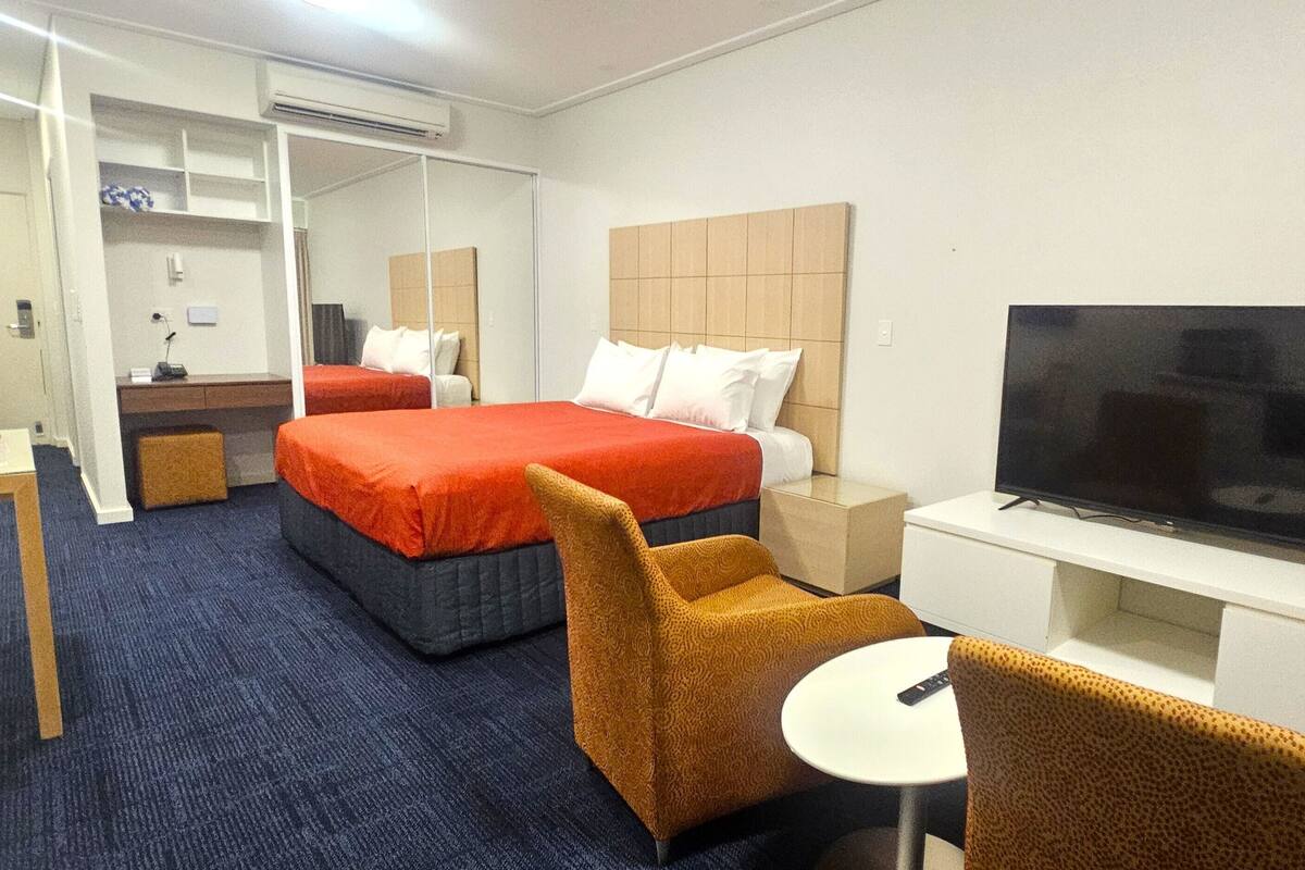 A hotel room with a bed, a TV, a desk, and a chair.