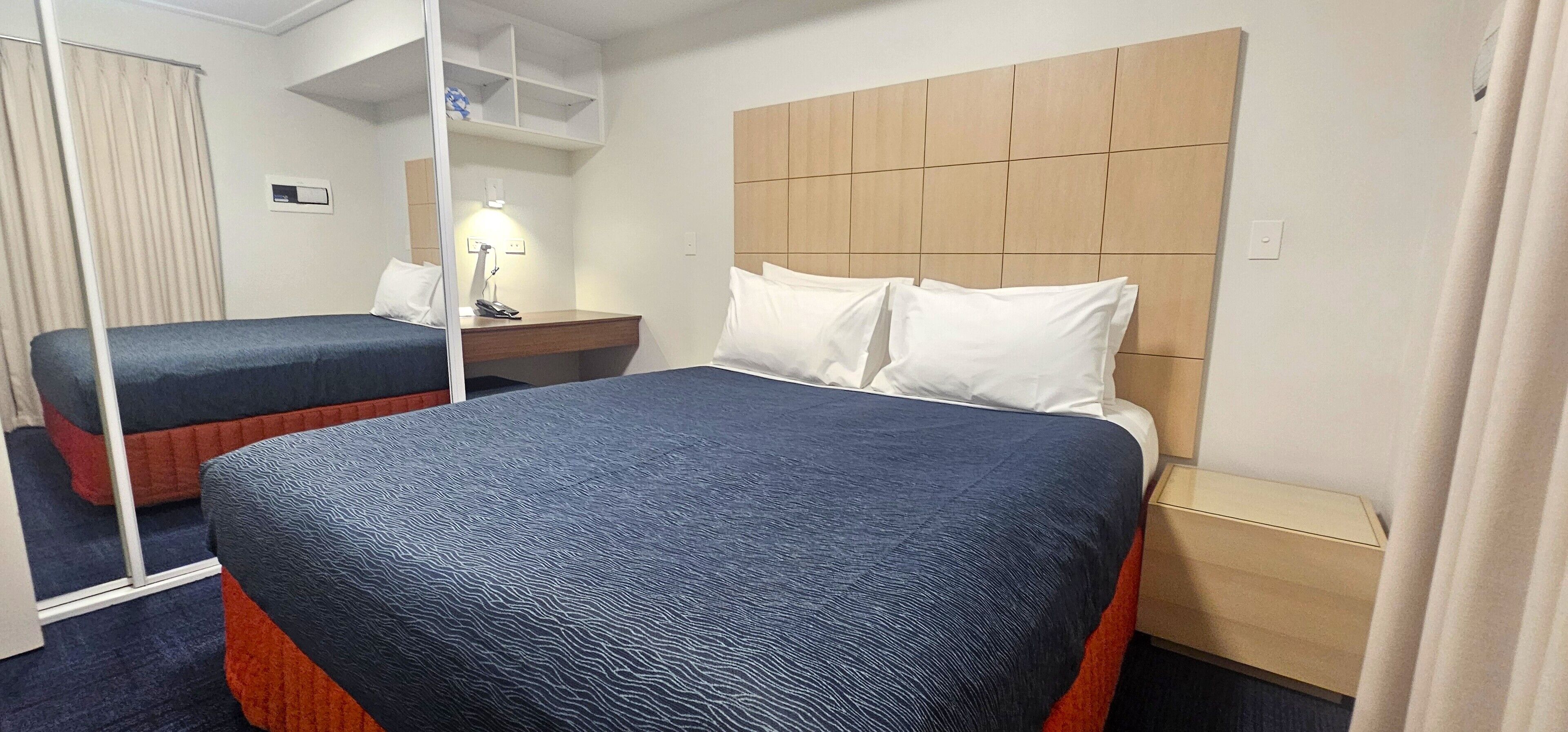A hotel room with two beds, a wooden headboard, a desk with a lamp, and a mirror.
