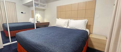 A hotel room with two beds, a wooden headboard, a desk with a lamp, and a mirror.
