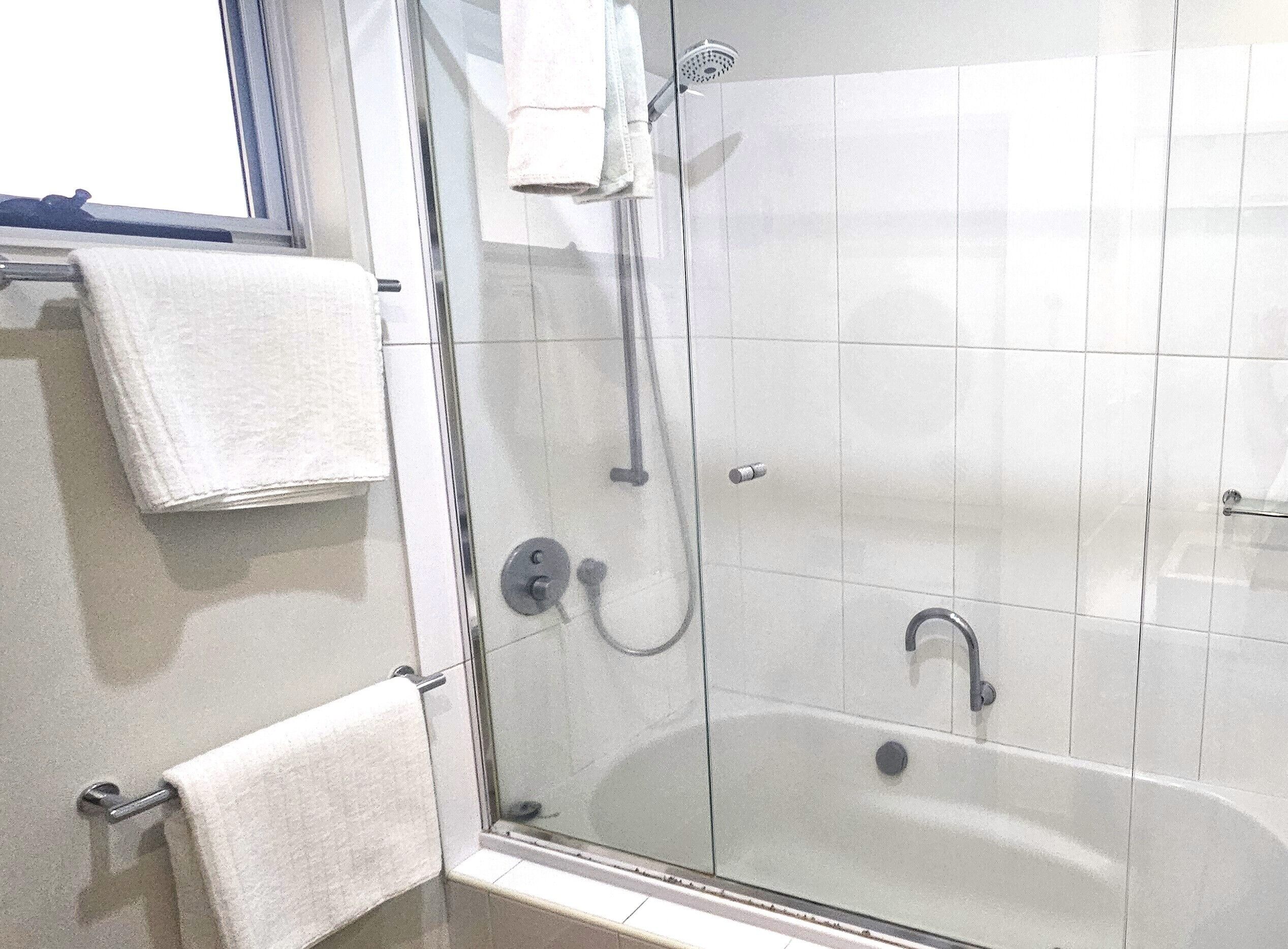 A glass-enclosed shower area with a handheld showerhead and a wall-mounted faucet.