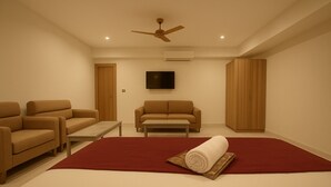 A modern living room with a large red rug, two sofas, a coffee table, a TV, and a ceiling fan. - Hotel Om Vilas (Mathura)