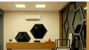 A reception desk with a wooden finish, two hexagonal mirrors, a small refrigerator, and a large window with a geometric pattern. - Hotel Om Vilas (Mathura)