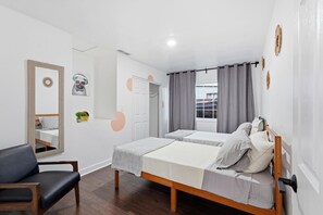 A modern hotel room with two single beds, a wooden chair, a mirror, and a view of the street.