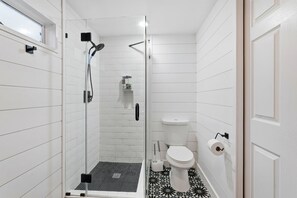 A modern bathroom with a glass-enclosed shower, white tiled walls, and a patterned floor.