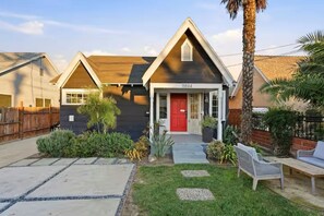 A house with a red door, a number plaque, and a well-maintained garden with a bench.