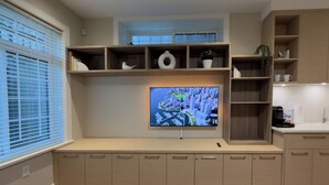 Et moderne køkken med indbyggede skabe, et fladskærms TV ophængt på væggen og et vindue med persienner.