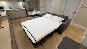 Et moderne soveværelse med seng, sofa, et lille bord og et tekøkken.