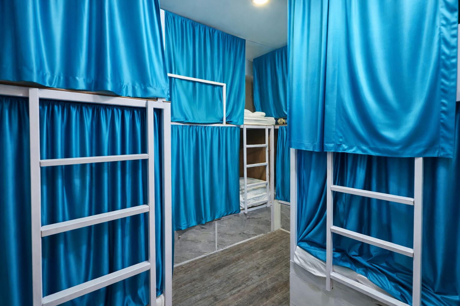 A room with bunk beds, blue curtains, and a small table with a lamp.