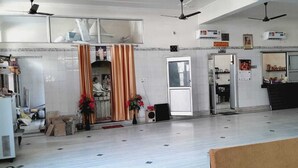 A spacious room with a tiled floor, ceiling fans, a large window, and a door leading to another room. - BABA SITARAM ASHRAM (Haridwar)