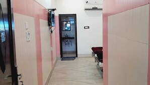 A narrow hallway with pink and white walls, a door at the end, and a bed with a red cover in the background. - BABA SITARAM ASHRAM (Haridwar)