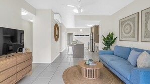 A modern living room with a TV, wooden cabinet, blue sofa, and a round coffee table. - Distinct at the Botanicals (Edge Hill)