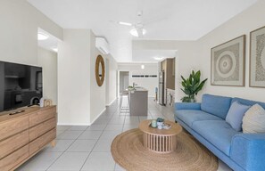 A modern living room with a TV, wooden cabinet, blue sofa, and a round coffee table.