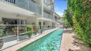 A modern apartment building with a swimming pool, outdoor seating, and lush greenery. - Distinct at the Botanicals (Edge Hill)