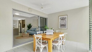 A dining area with a wooden table and white chairs, a sofa, and a framed picture on the wall. - Distinct at the Botanicals (Edge Hill)
