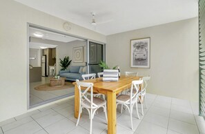 A dining area with a wooden table and white chairs, a sofa, and a framed picture on the wall.