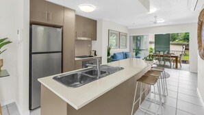 A modern kitchen with a central island, stainless steel appliances, and a dining area with outdoor seating. - Distinct at the Botanicals (Edge Hill)