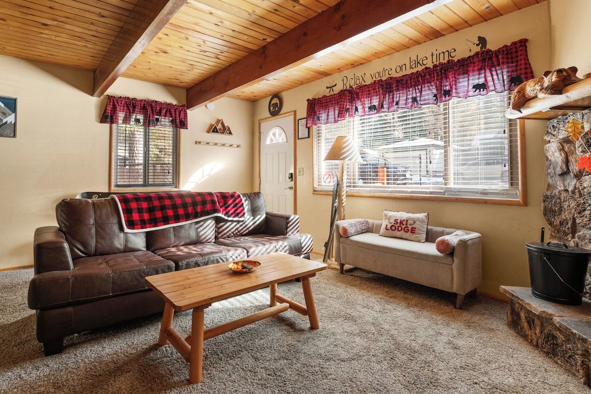 Una sala de estar acogedora con un sofá de cuero marrón, una mesa de centro de madera y un sofá cama con un cojín que dice 'SKI LODGE'.