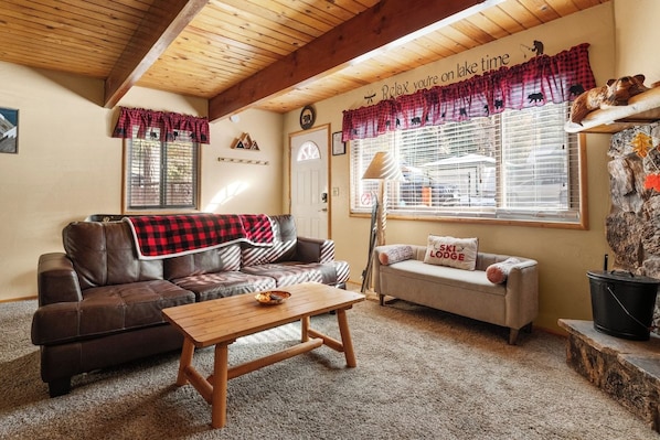 A cozy living room with a brown leather sofa, a wooden coffee table, and a sofa bed with a pillow labeled 'SKI LODGE'. - Grizzly Hollow - Close to Bear Mtn, & Alpine Zoo (Big Bear Lake)