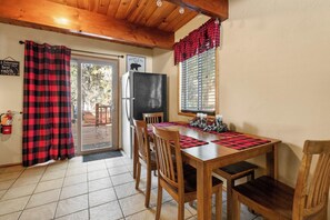 A dining area with a wooden table, chairs, a refrigerator, and a window with blinds. - Grizzly Hollow - Close to Bear Mtn, & Alpine Zoo (Big Bear Lake)