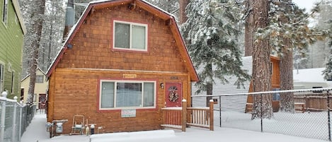A wooden cabin with a red door, a window, and a chimney.