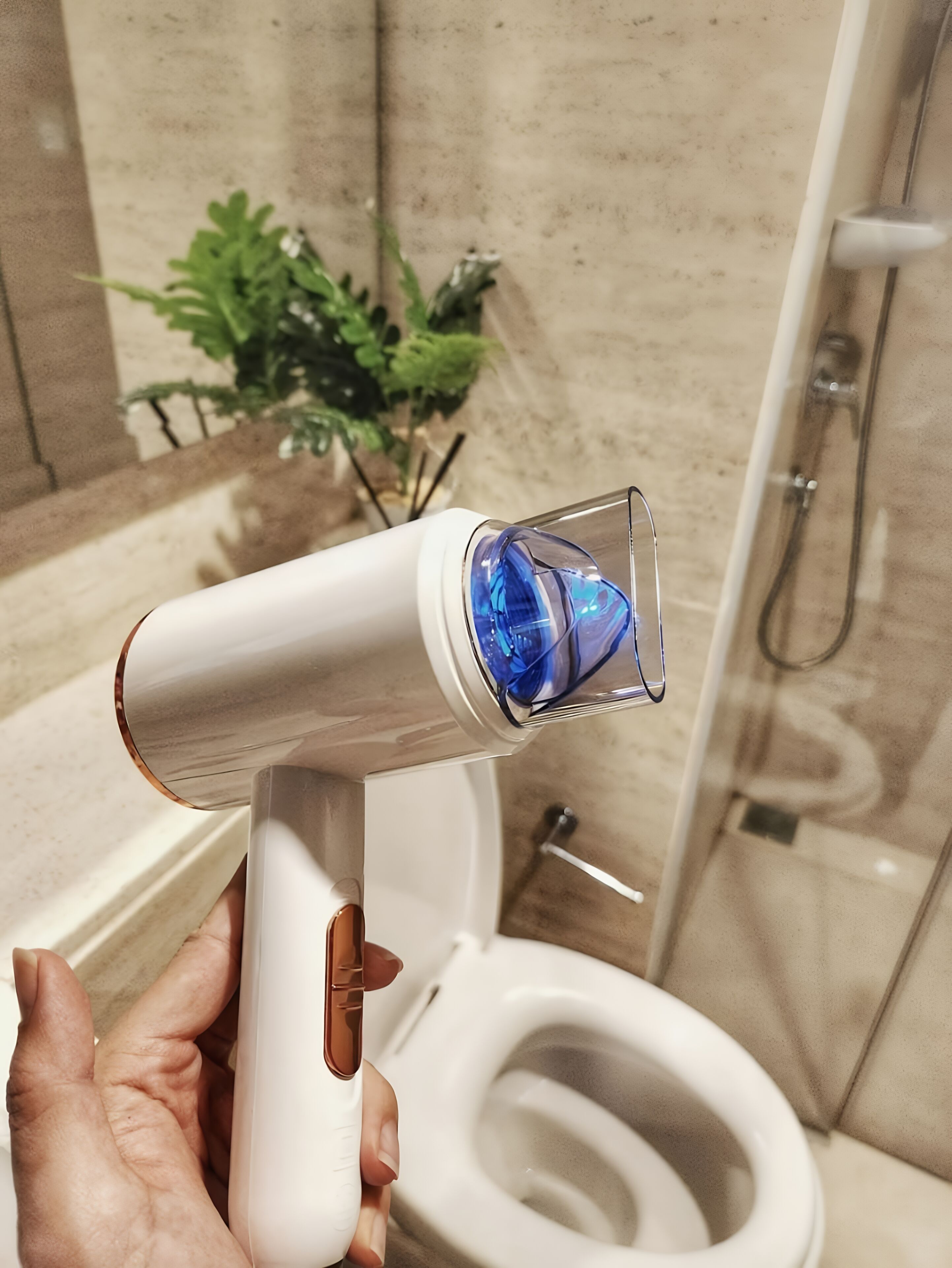 A bathroom with a toilet, a shower, and a hand holding a hairdryer.