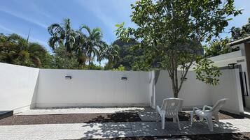 Un patio con una pared blanca, un árbol pequeño y dos sillas de plástico blancas.
