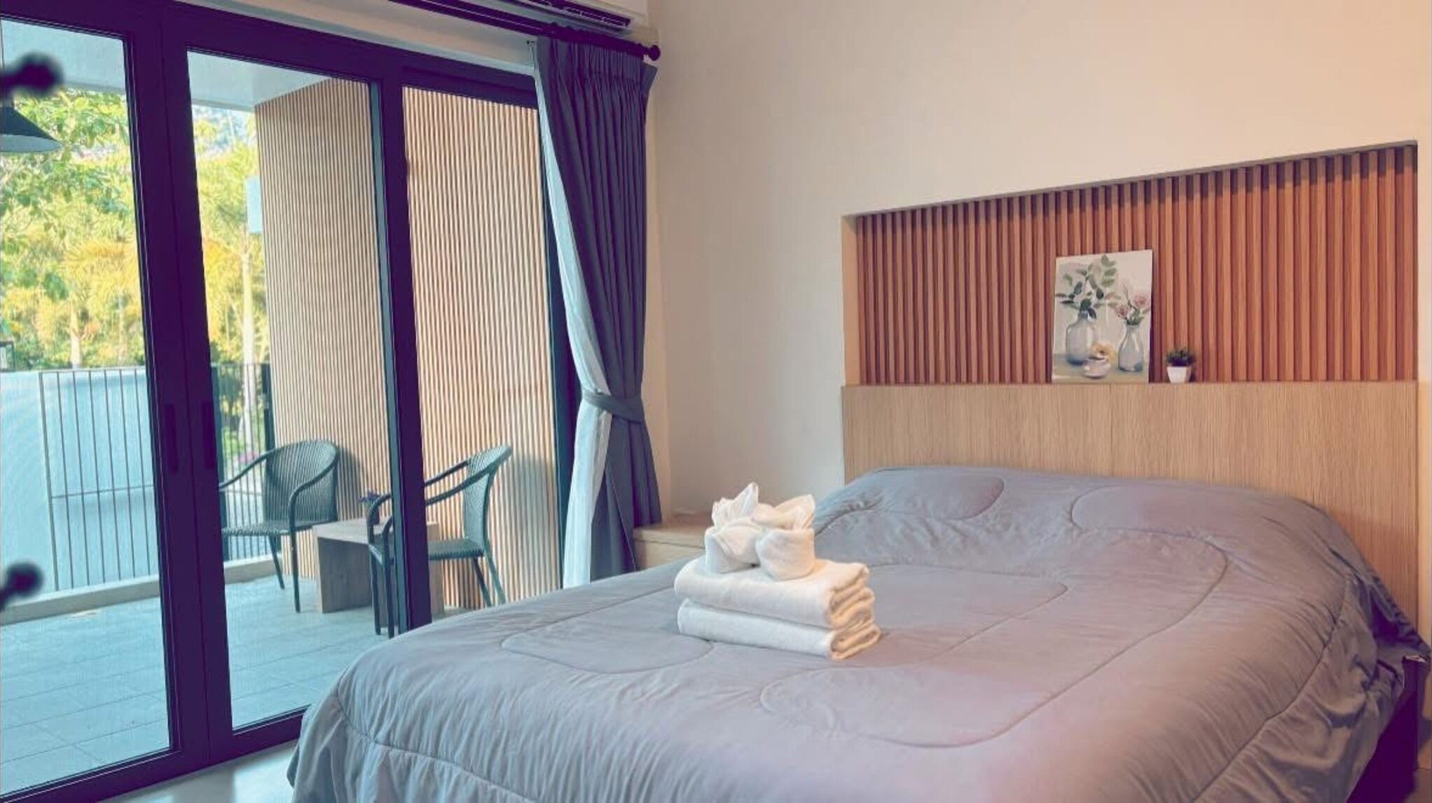 A bedroom with a large bed, a sliding glass door to a balcony, and a wooden headboard.