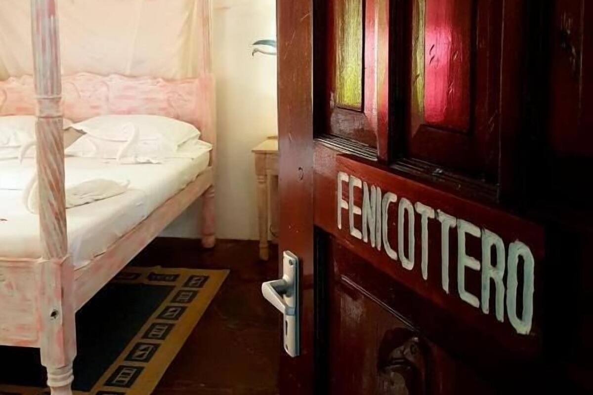 Une pièce avec un lit, une porte en bois portant l’inscription « FENICOTTERO », et une petite table.