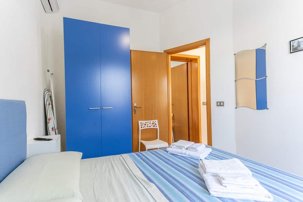 A bedroom with a bed, a blue wardrobe, a chair, and a towel rack.