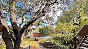 A stone pathway leading through a garden with a large tree, a wooden staircase, and a lamp post. - Apartment in Galapagar With Pool and Garden (Galapagar)