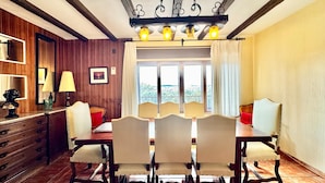 A dining area with a wooden table and chairs, a chandelier, and a view through the window. - Apartment in Galapagar With Pool and Garden (Galapagar)