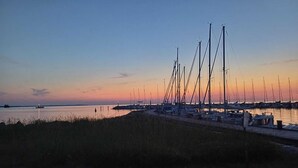 A marina with multiple sailboats docked, a calm water body, and a grassy foreground. - Feriendomizile auf der Insel Poel (Insel Poel)
