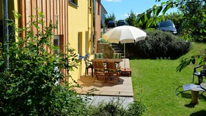 A wooden deck with outdoor furniture, a white umbrella, and a stone wall. - Feriendomizile auf der Insel Poel (Insel Poel)