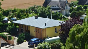 A yellow house with a grey roof, surrounded by greenery and a large field in the background. - Feriendomizile auf der Insel Poel (Insel Poel)