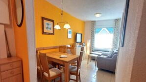 A dining area with a wooden table and chairs, a television, and a sofa in the background. - Feriendomizile auf der Insel Poel (Insel Poel)