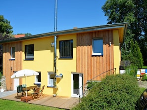 A yellow building with wooden paneling, a deck with outdoor furniture, and a staircase leading to a door. - Feriendomizile auf der Insel Poel (Insel Poel)